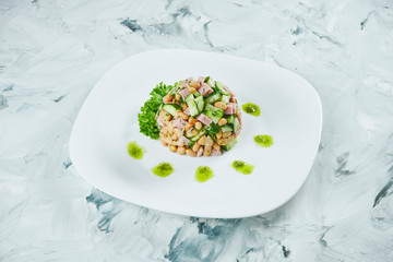 Portion of fresh and healthy Salad with beans, ham and pickled mushrooms, seasoned with pesto on white plate. Grey background.