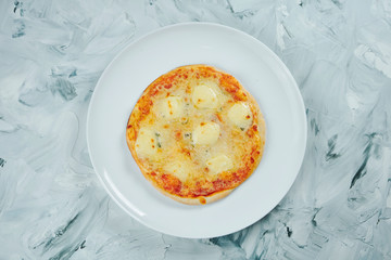 A small portion of children's pizza 4 cheese with mozzarella and blue cheese with mold on white plate on grey background
