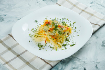 Portion of homemade Italian lasagna with cheese, white sauce and chicken on white plate with cloth. Traditional italian pasta. Grey background
