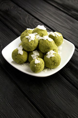 Energy balls with  matcha powder, pistachios, dates  and coconut chips in the white plate on the black  wooden background. Location vertical.