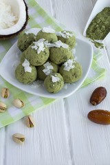 Energy balls with  matcha powder, pistachios, dates  and coconut chips in the white plate on the white wooden background. Location vertical.