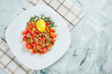 Homemade summer salad with tomatoes, olive oil and baked veal on a white plate on a gray background.
