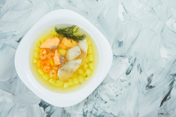 Homemade transparent fish soup with sea bass, salmon and shrimp in a white bowl on a gray background. Seafood