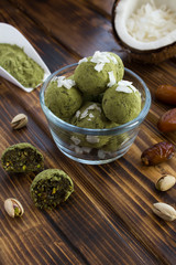 Energy balls with  matcha powder, pistachios, dates  and coconut chips in the glass bowl  on the brown  wooden background. Location vertical.