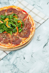 Italian juicy homemade pizza with vitello tonato veal and spinach leaves with red sauce and mozzarella on grey background.