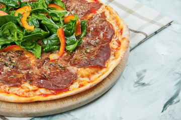 Italian juicy homemade pizza with vitello tonato veal and spinach leaves with red sauce and mozzarella on grey background.