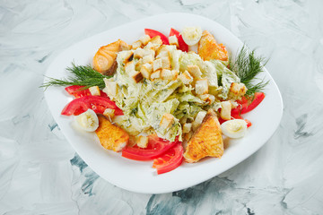 Portion of Caesar salad with croutons, lettuce, white sauce and fried salmon in white plate on grey background. Healthy restaurant food