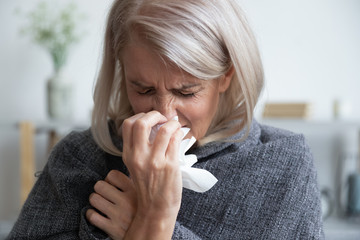 Ill mature woman covered with blanket blowing running nose sneeze