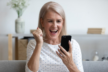 Overjoyed mature woman holding phone feeling excited about mobile win