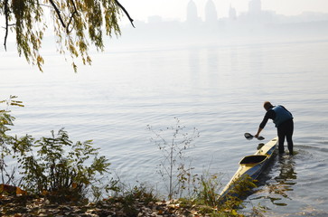 Autumn day. A sportsman in a life jacket stands in the water near a kayak boat.