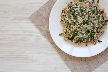 Homemade mushroom risotto on a white plate on a white wooden surface, top view. Overhead, from above, flat lay. Space for text.