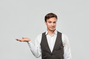 Handsome man in a white shirt and grey vest holding palm of a hand for product placement or advertising.