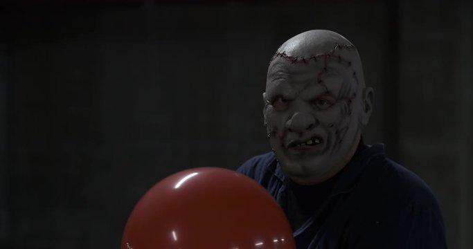 In dark basement there is man with red ball, he hits him with bat and angrily looks at camera, prepares for attack, actor plays monster in production, Halloween, phobia and shock, psycho and ball