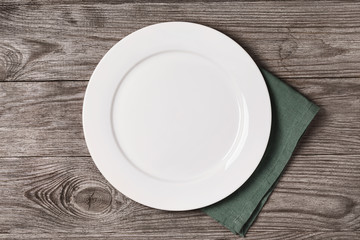 Empty ceramic plate with green napkin on a wooden table, top view. Food background