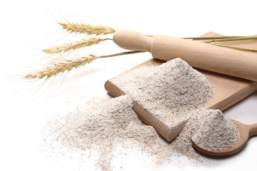 Integral rye flour pile with dry ears wheat grain, spoon, chopping board and wooden rolling pin...
