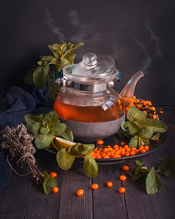 Herbal Tea with sea buckthorn and mint in a glass teapot, selective focus, rustic background. Cold medicine. Folk medicine