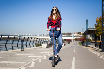 Pretty young woman riding an electric scooter in the street