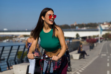 Pretty young woman riding an electric scooter in the street