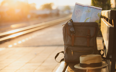 Map in Backpack ,Mobile phone with earphone and hat at the train station with a traveler.sun set,...