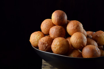 Round golden donuts in a ceramic bowl on the edge of the wooden table against black background