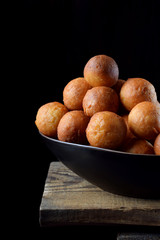 Round golden donuts in a ceramic bowl on the edge of the wooden table against black background