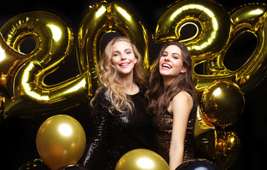 Happy gorgeous girls in stylish sexy party dresses holding gold 2020 balloons, having fun at New...