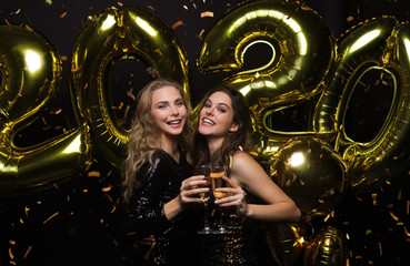 Happy gorgeous girls in stylish sexy party dresses holding gold 2020 balloons, having fun at New...