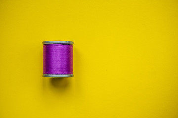 Wooden, purple reel of thread on yellow background. Minimal aesthetics.