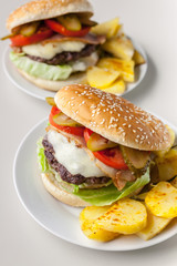 Two homemade hamburgers with a juicy meat cutlet, parmesan cheese, green salad, tomatoes and fried potatoes on a light background. Vertical shot