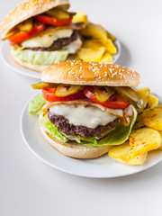 Two homemade hamburgers with a juicy meat cutlet, parmesan cheese, green salad, tomatoes and fried potatoes on a light background. Vertical shot