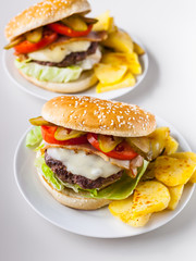 Two homemade hamburgers with a juicy meat cutlet, parmesan cheese, green salad, tomatoes and fried potatoes on a light background. Vertical shot