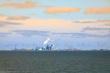 Factories and a coal-fired power plant surrounded by wind turbines