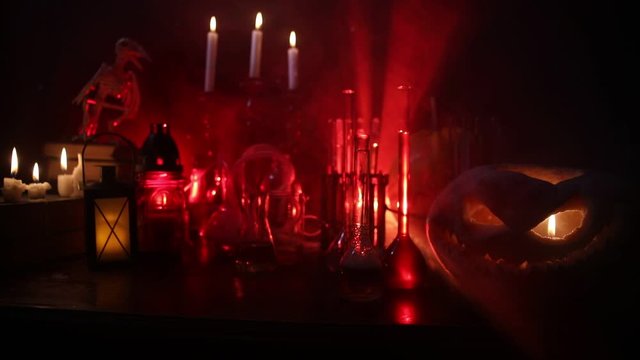 Wizard's Desk. Horror Halloween concept. Magic potions in bottles on wooden table with books and candles. Halloween still-life background with different elements on dark toned foggy background. Select