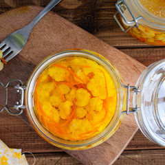 Pickled cauliflower with carrots in glass jars on a wooden table, square, top view