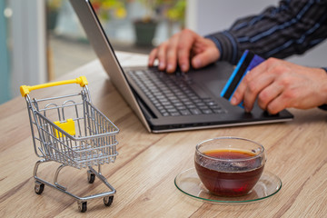 Internet shopping.  Thumbnail of a shopping trolley with laptop, bank card and glass of tea. ...