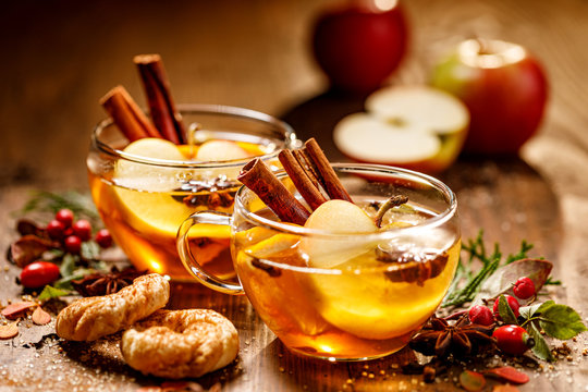 Mulled cider with apple slices, cinnamon sticks, cloves, anise stars and citrus fruits in glass cups on a wooden rustic table. Delicious, traditional hot drink