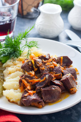Braised beef heart with mashed potatoes and pickles on a white plate, selective focus