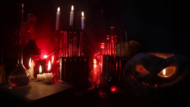 Wizard's Desk. Horror Halloween concept. Magic potions in bottles on wooden table with books and candles. Halloween still-life background with different elements on dark toned foggy background. Select