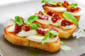 Tasty savory Italian appetizers, or bruschetta, on slices of toasted baguette garnished with basil