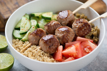 Close-up of a food bowl with meatball skewers, quinoa, bulgur and fresh vegetables, selective focus