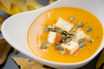 Cream-soup with pumpkin and addition of fried cheese and pumpkin seeds served in a white bowl, close-up, selective focus