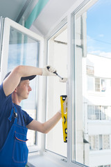worker corrects the window frame with a rubber hammer and checks the yellow level