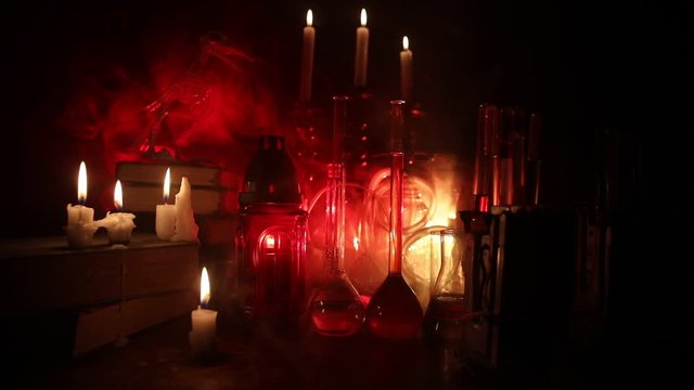 Wizard's Desk. Horror Halloween concept. Magic potions in bottles on wooden table with books and candles. Halloween still-life background with different elements on dark toned foggy background. Select