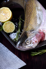 Fresh raw lacustrine trout on black tray with sea salt, lemon, lime and rosemary