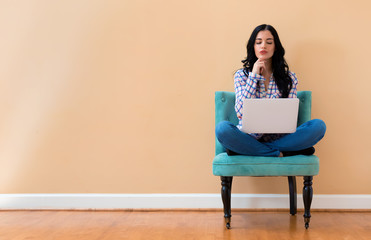 Young woman with a laptop computer in a thoughtful pose sitting in a chair