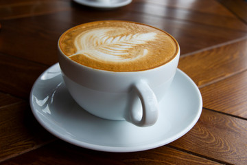 A large mug of fragrant cappuccino, on a saucer and a wooden table.