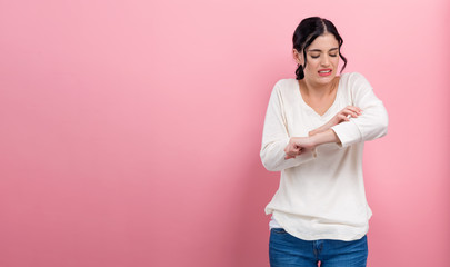 Young woman scratching her itchy arm. Skin problem. on a pink background