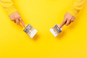 Paint brush in the hand of a girl on a yellow background, concept of apartment repair and painting...