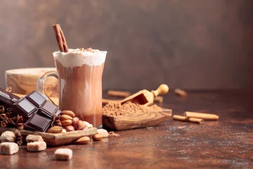 Fototapeten Hot chocolate with cocoa powder, cream, cinnamon, chocolate pieces and other ingredients on a brown table. © Igor Normann