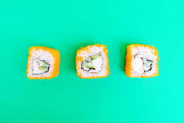 Rolls with tobiko caviar, cucumber and crab meat on a bright green background. Minimalistic stylish japanese food concept. Flat lay, top view. Copy space.